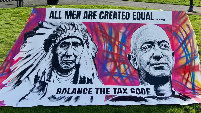 An art piece showing Chief Seattle and Jeff Bezos next to each other, text on the painting says "All men are created equal... balance the tax code"