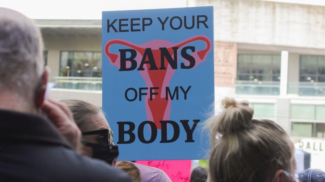 A protest sign with a uterus reads "keep your bans off my body"