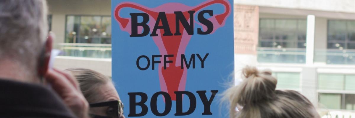 A protest sign with a uterus reads "keep your bans off my body"