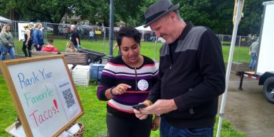 A volunteer explains ranked choice voting to a voter at a community event